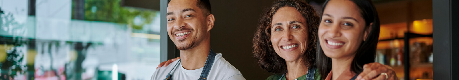 three store workers in aprons smiling at the camera 